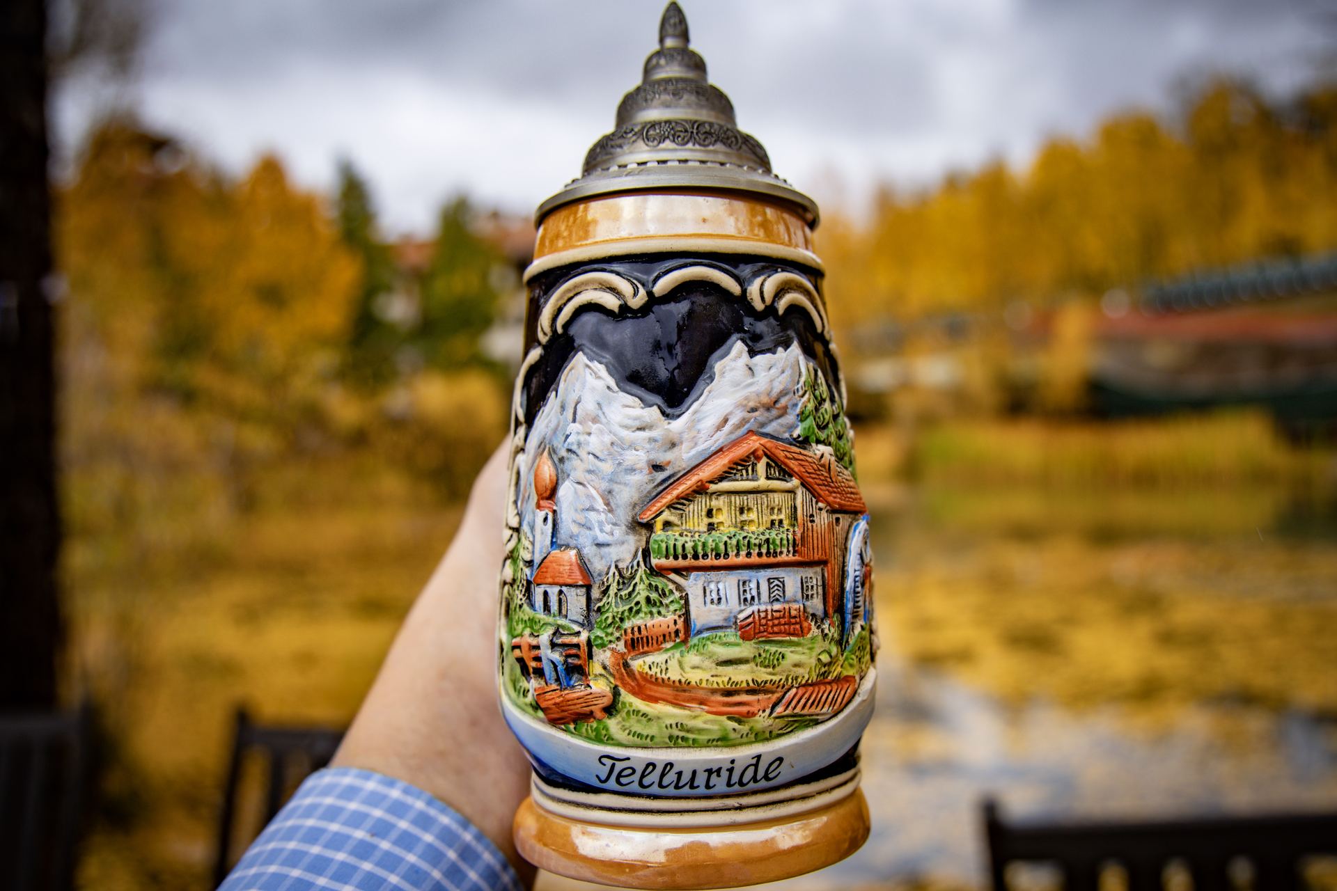 A ceramic Telluride souvenir beer stein held up against golden aspen trees