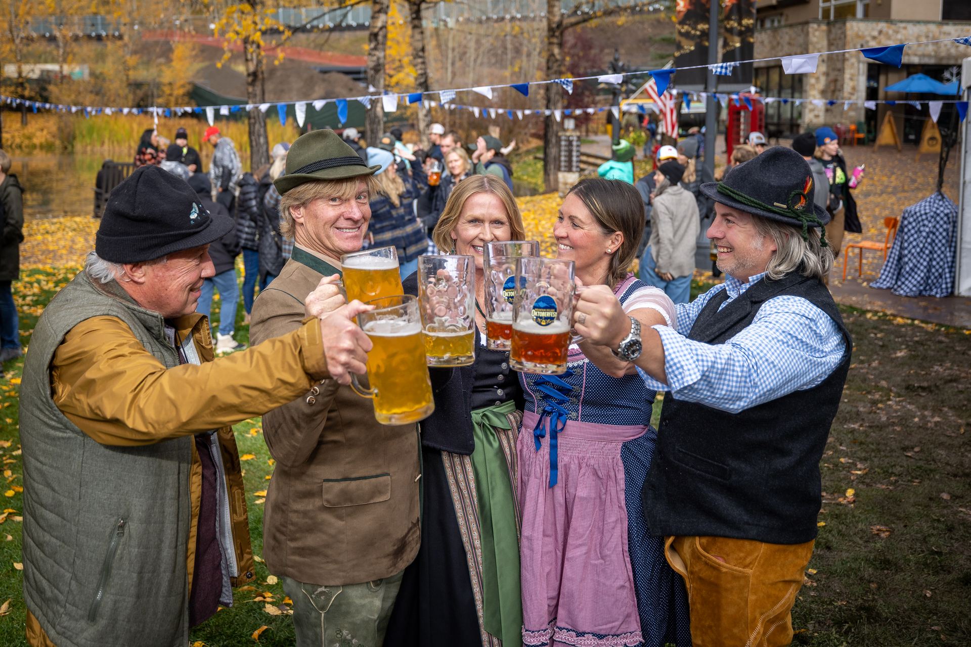 A group of friends clinking beer steins together in the plaza among golden aspens