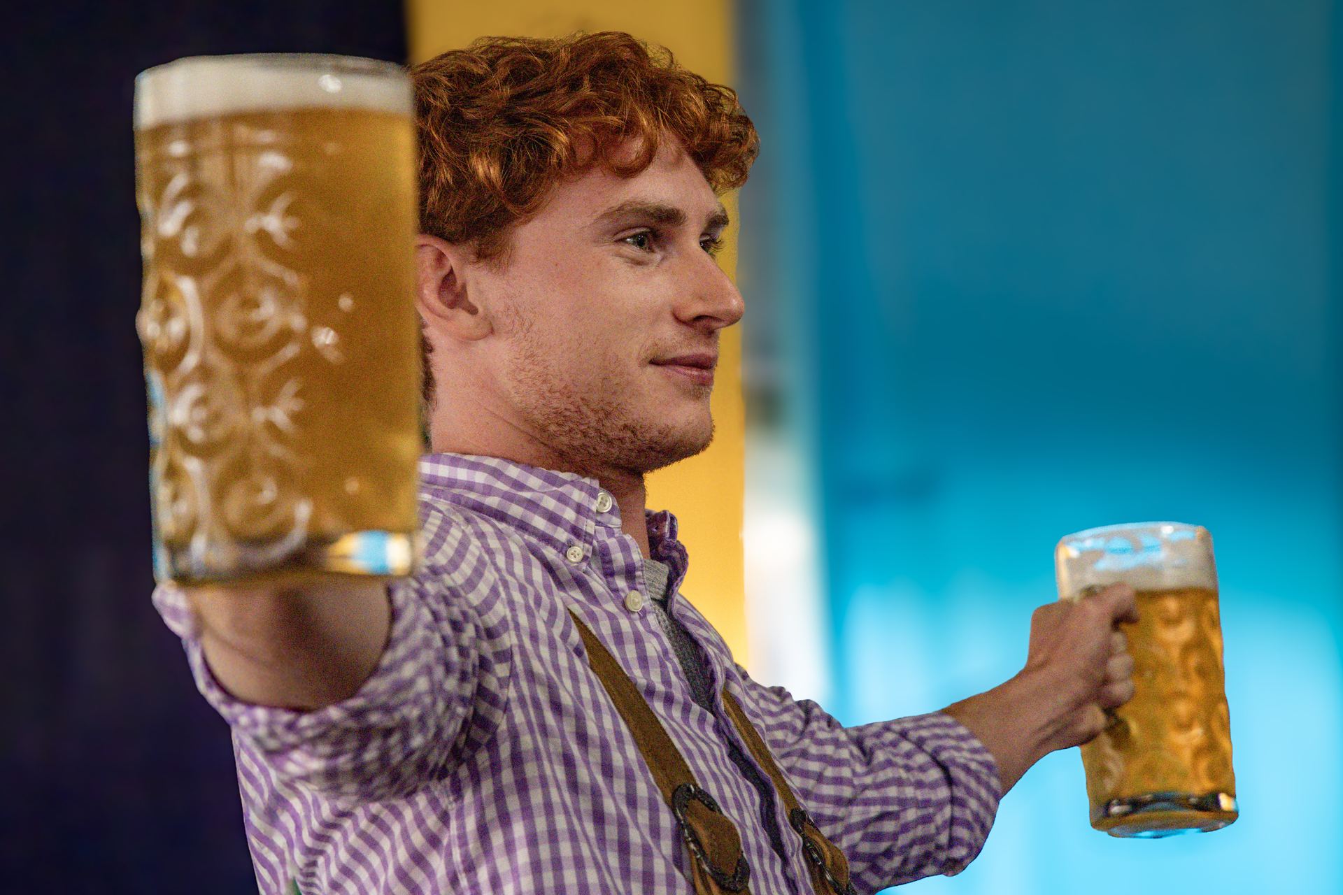 A festival guest raising two beer mugs in a toast under the tent
