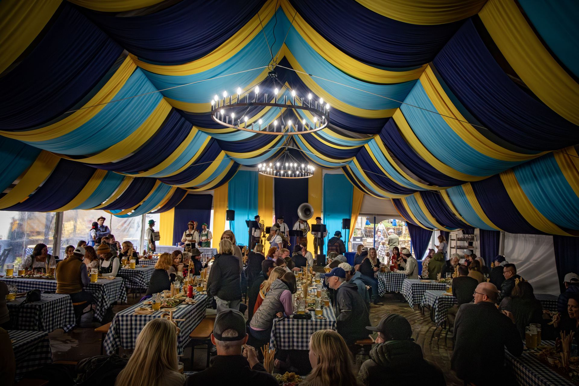Inside the festival tent, guests gather at long gingham-clothed tables beneath string-lit chandeliers